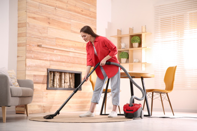 Photo of Young woman using vacuum cleaner at home