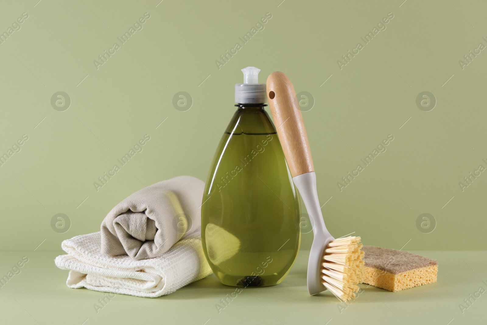 Photo of Bottle of cleaning product, sponge, rags and brush on light green background