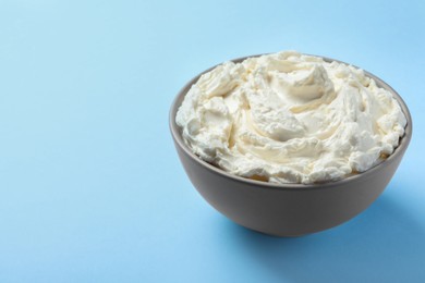 Photo of Bowl of tasty cream cheese on light blue background, space for text