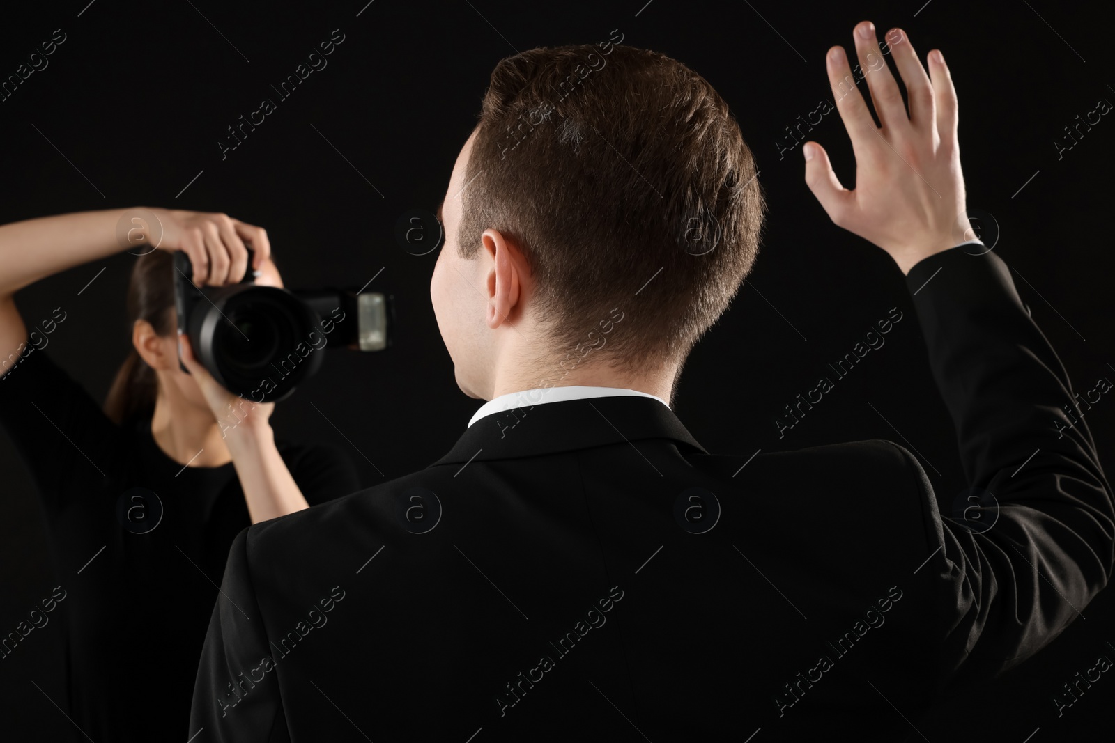 Photo of Professional photographer taking picture of man on black background, selective focus