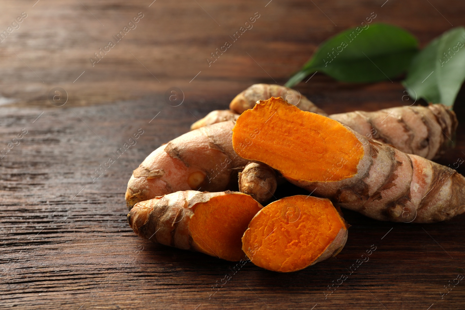 Photo of Fresh turmeric roots on wooden table, closeup. Space for text