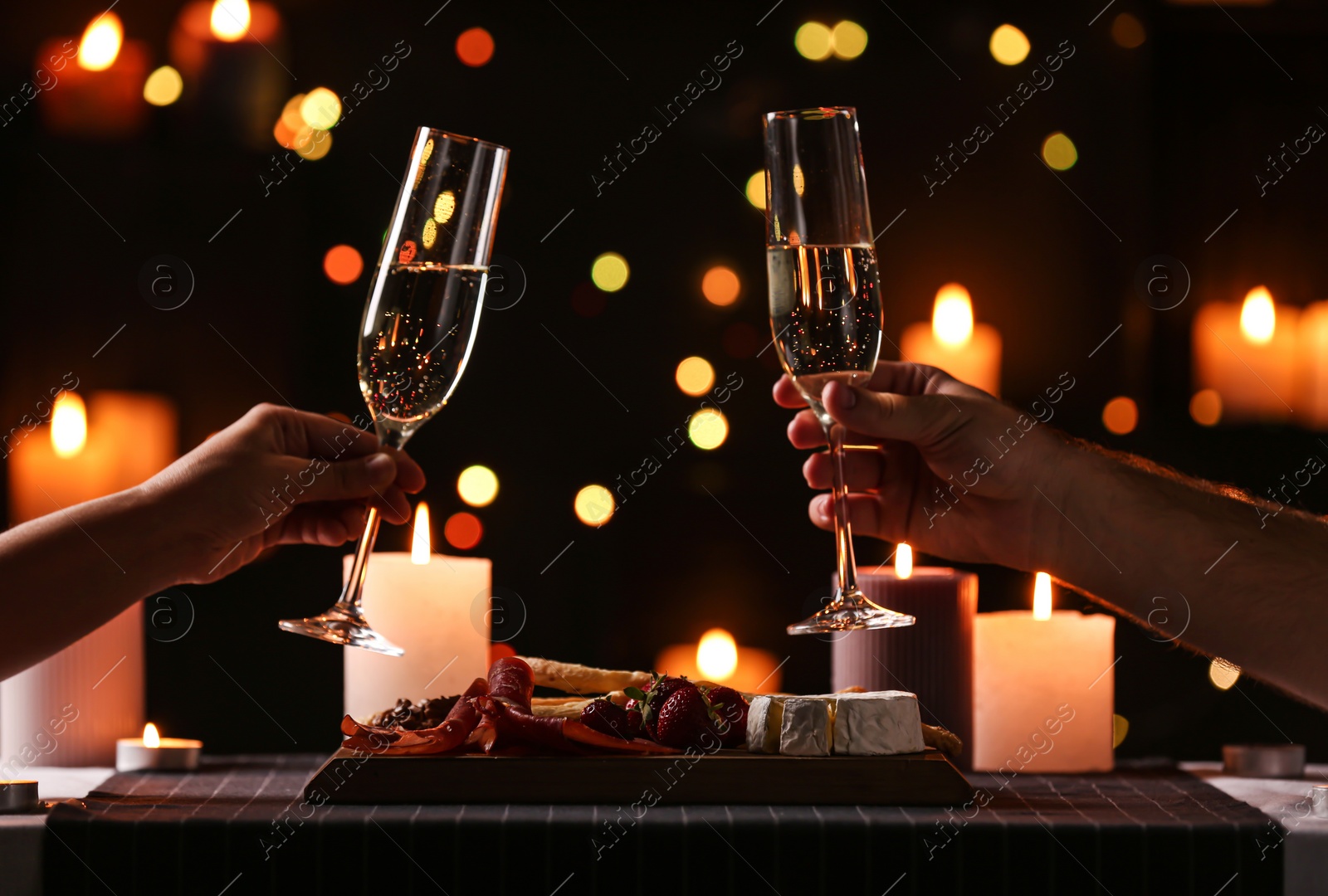 Photo of Young couple with glasses of champagne having romantic candlelight dinner at table, closeup