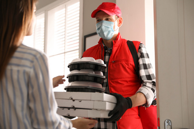 Photo of Courier giving orders to woman indoors. Food delivery service during coronavirus quarantine