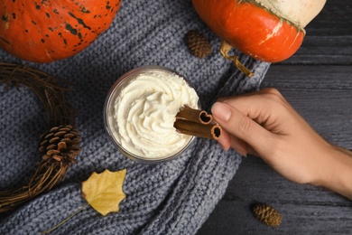 Photo of Woman holding cup with pumpkin spice latte on wooden background, top view