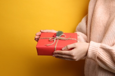 Woman holding Christmas gift box on yellow background, closeup