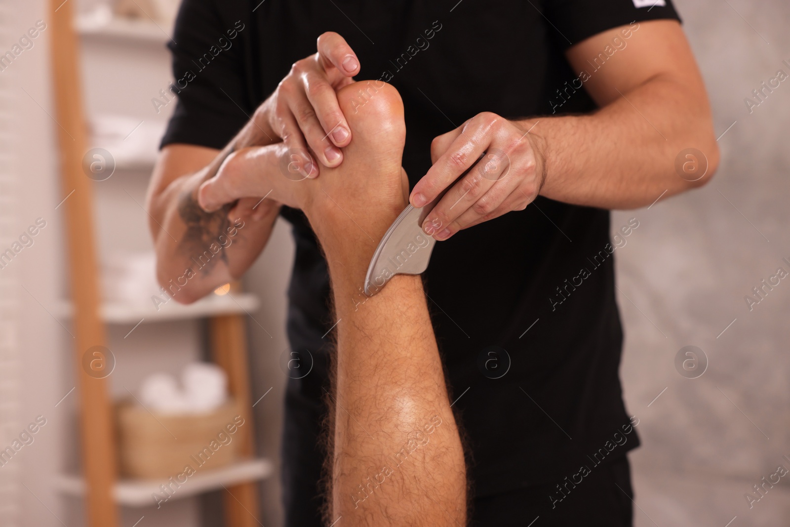 Photo of Man receiving professional leg massage with gua sha tool in spa salon, closeup