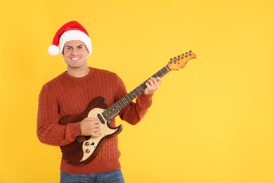 Photo of Man in Santa hat playing electric guitar on yellow background, space for text. Christmas music