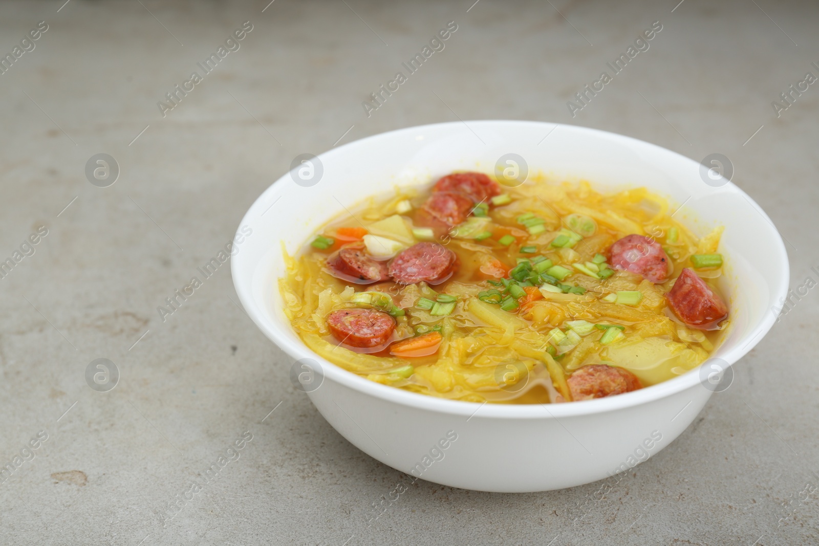 Photo of Delicious sauerkraut soup with smoked sausages and green onion on light grey table