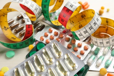 Photo of Many different weight loss pills and measuring tape on white wooden table, closeup