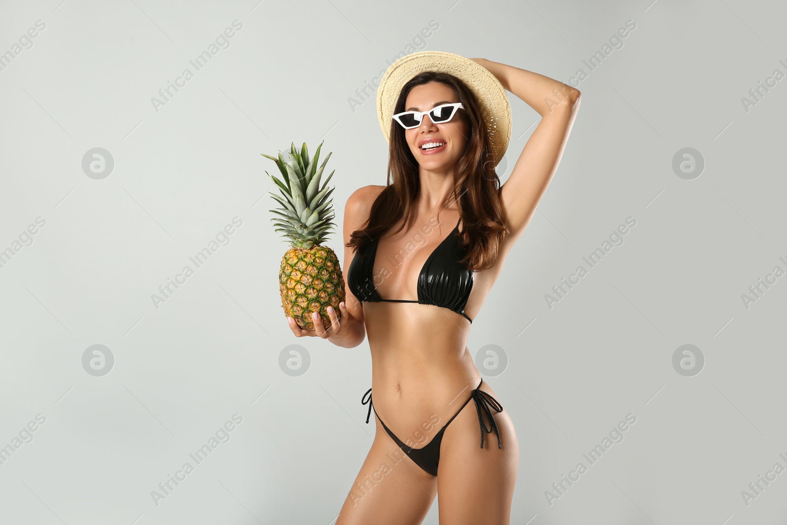 Photo of Beautiful woman in stylish bikini with pineapple on light grey background