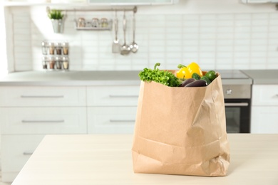 Photo of Paper shopping bag full of vegetables on table in kitchen. Space for text