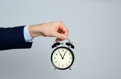 Photo of Closeup view of businessman holding alarm clock on grey background, space for text. Time management