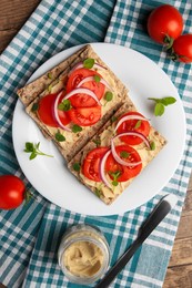 Fresh crunchy crispbreads with pate, tomatoes, red onion and greens on wooden table, flat lay