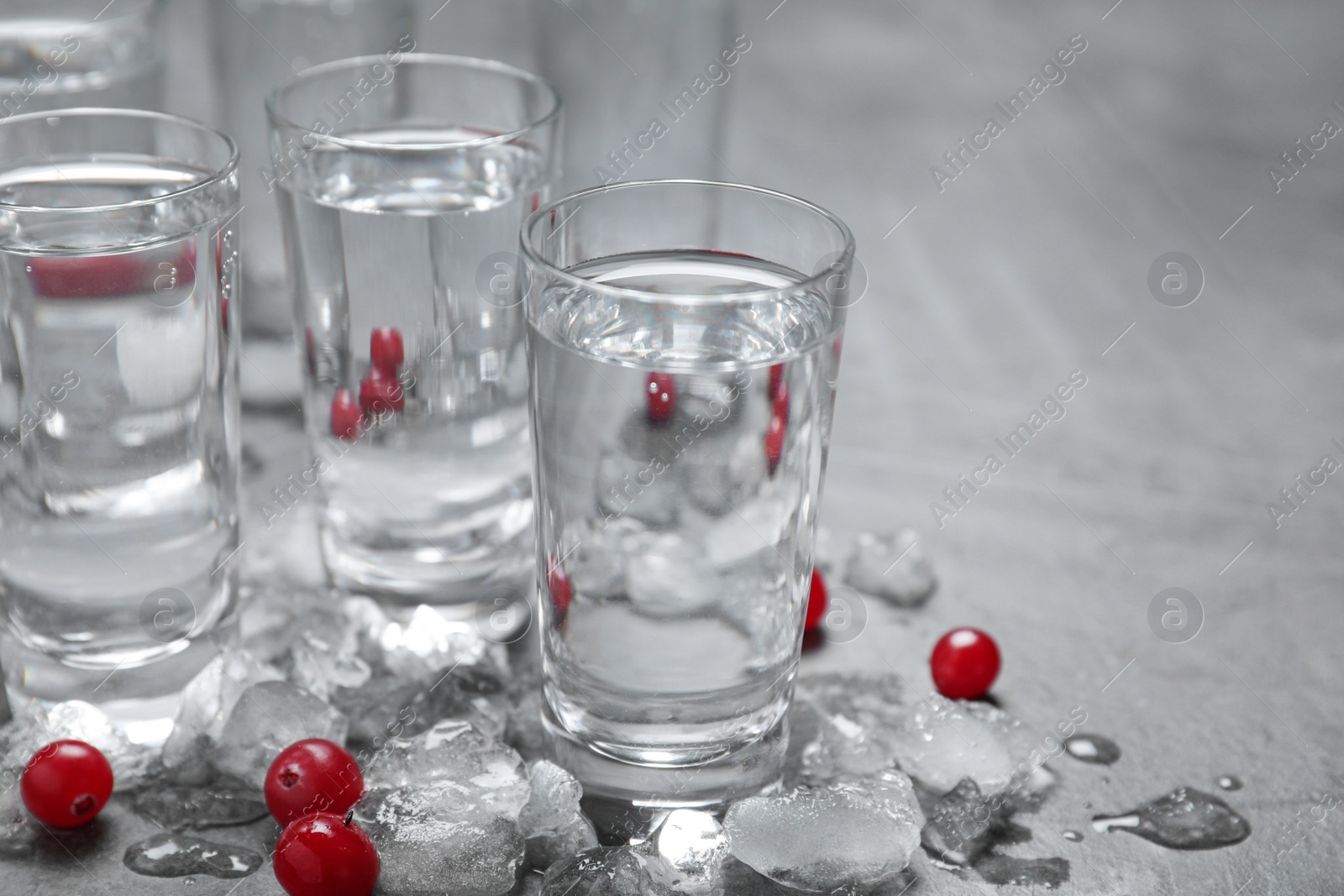 Photo of Shots of vodka, cranberries and ice on grey table