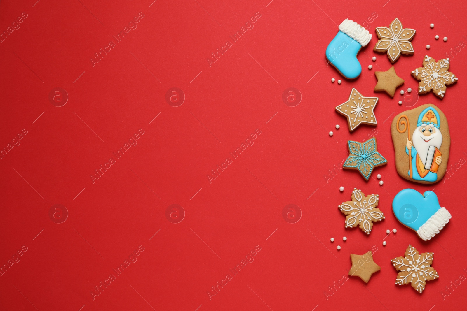 Photo of Tasty gingerbread cookies on red background, flat lay with space for text. St. Nicholas Day celebration