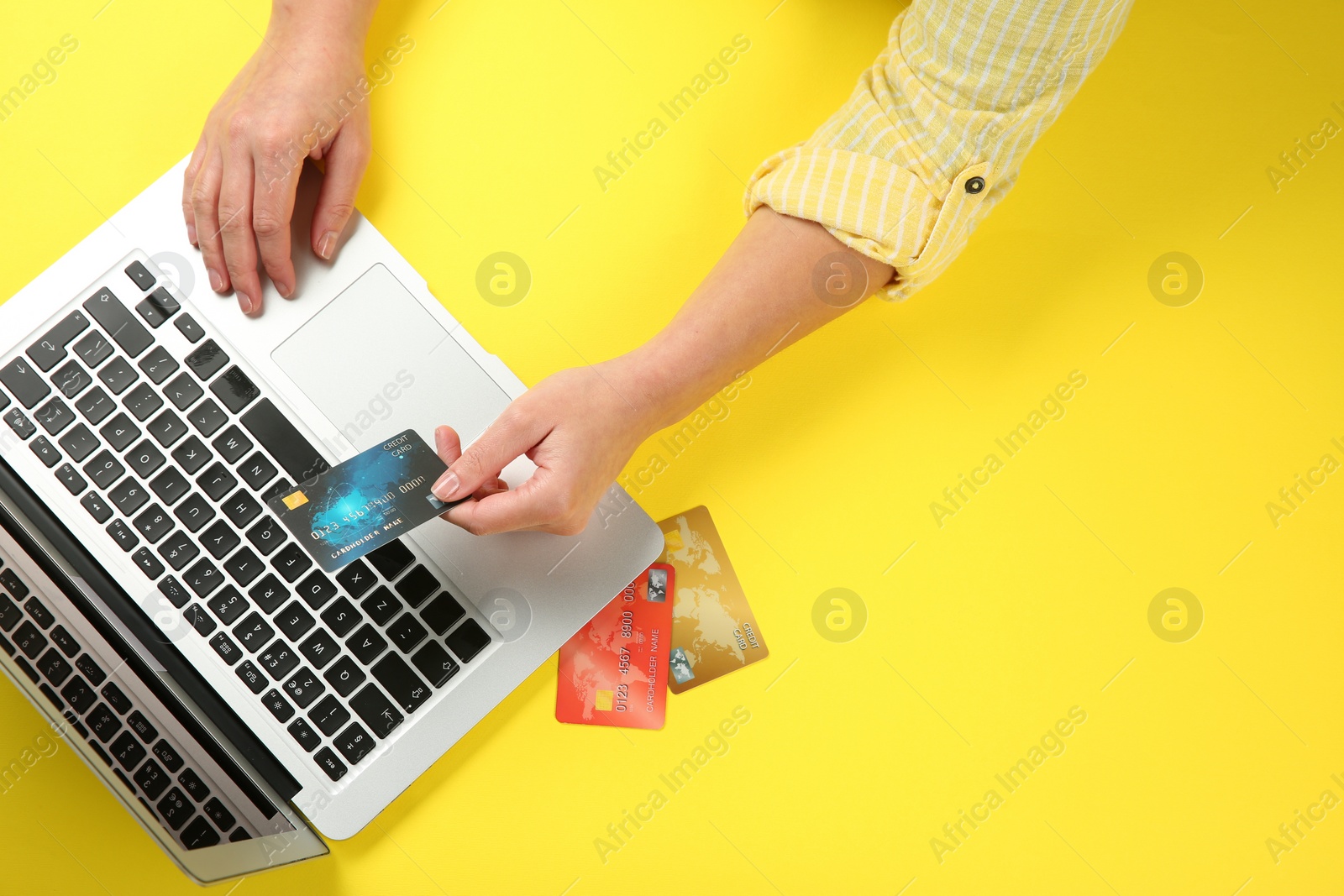 Photo of Online payment. Woman using credit card and laptop at yellow table, top view
