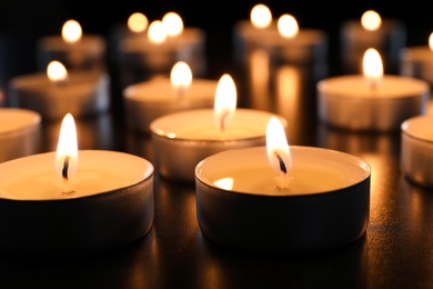 Wax candles burning on table in darkness, closeup