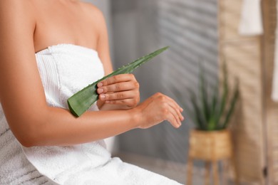 Young woman applying aloe gel onto her arm in bathroom, closeup. Space for text