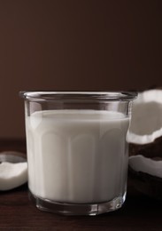 Glass of delicious vegan milk and coconut pieces on wooden table