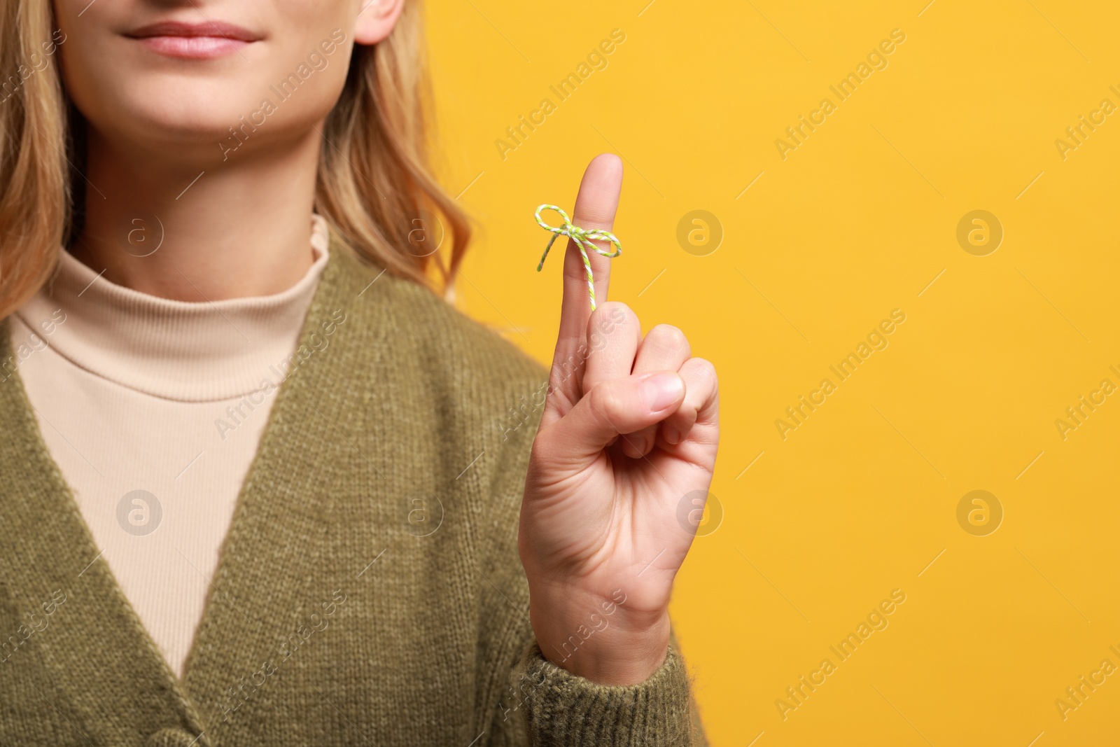 Photo of Woman showing index finger with tied bow as reminder on orange background, closeup