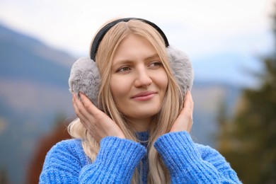 Photo of Young beautiful woman wearing warm earmuffs in mountains