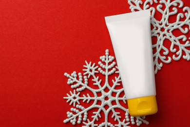 Photo of Tube of hand cream and snowflakes on red background, flat lay with space for text. Winter skin care