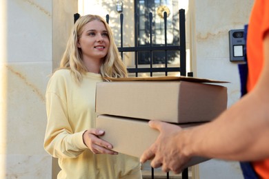 Photo of Young woman receiving parcels from courier outdoors