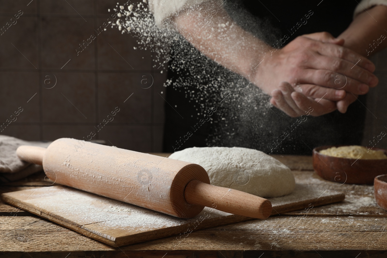 Photo of Man sprinkling flour over dough at wooden table, closeup