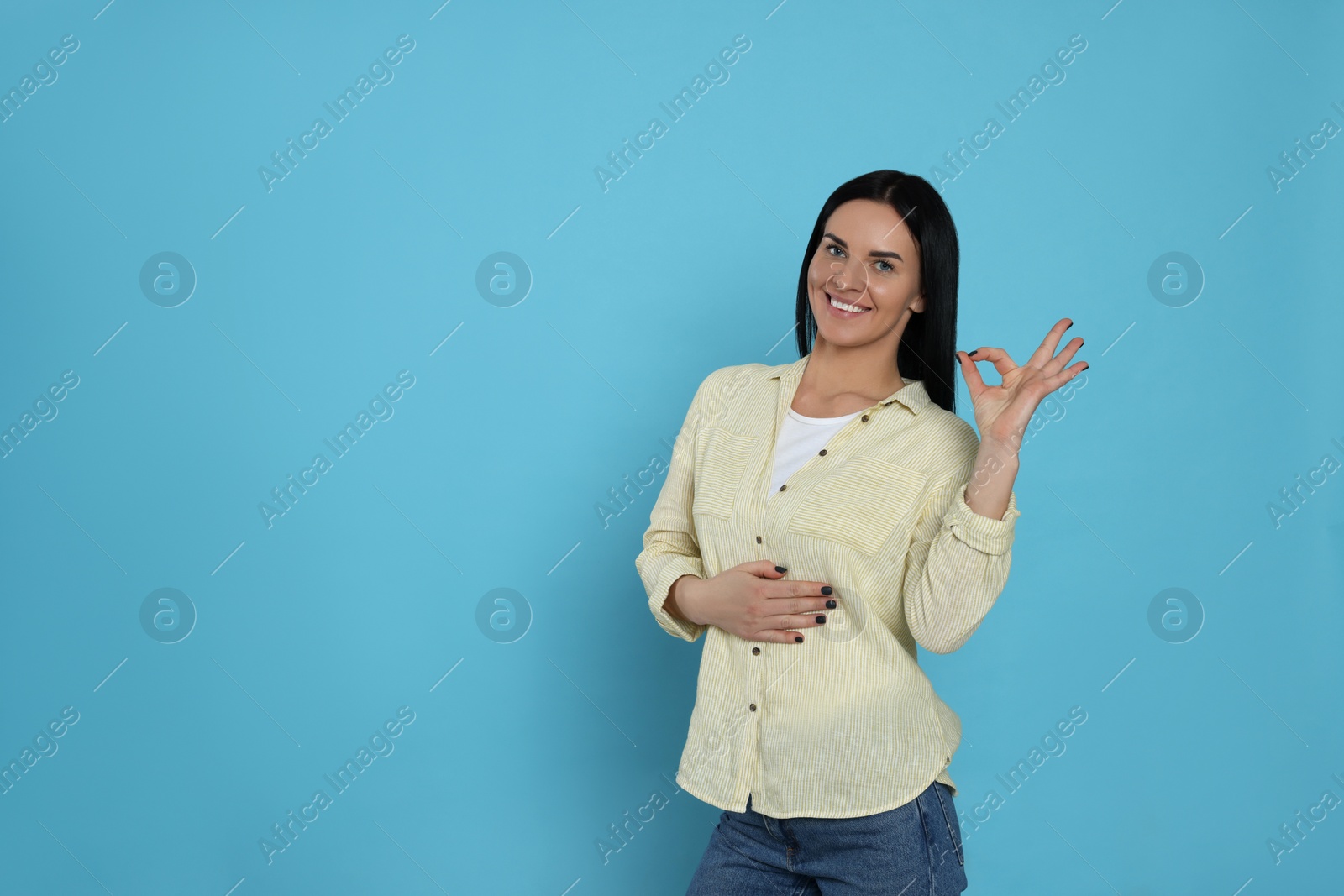 Photo of Happy woman touching her belly and showing okay gesture on light blue background, space for text. Concept of healthy stomach