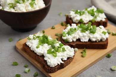 Photo of Bread with cottage cheese and green onion on light grey table, closeup