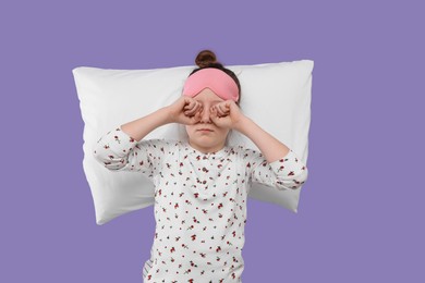 Girl with sleep mask and pillow rubbing her eyes on purple background. Insomnia problem