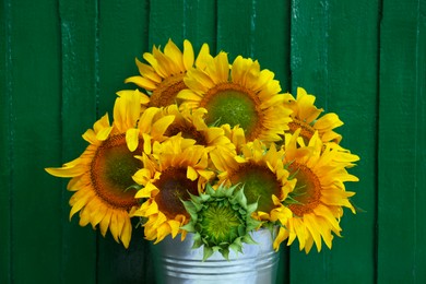 Bouquet of beautiful sunflowers in bucket near green wall, closeup