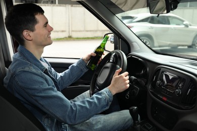 Smiling man with bottle of beer driving car. Don't drink and drive concept