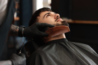 Photo of Professional hairdresser working with bearded client in barbershop, closeup
