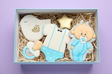 Set of baby shower cookies in gift box on lilac background, top view