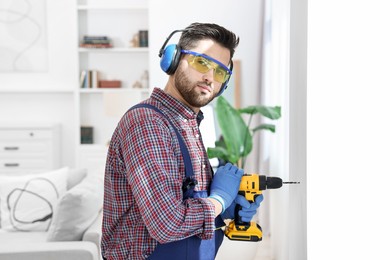 Young worker in uniform using electric drill indoors