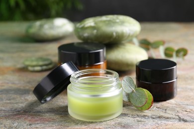 Photo of Jars of cream and eucalyptus leaves on textured table, closeup. Body care products