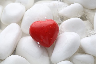 Red decorative heart on stones and water, closeup