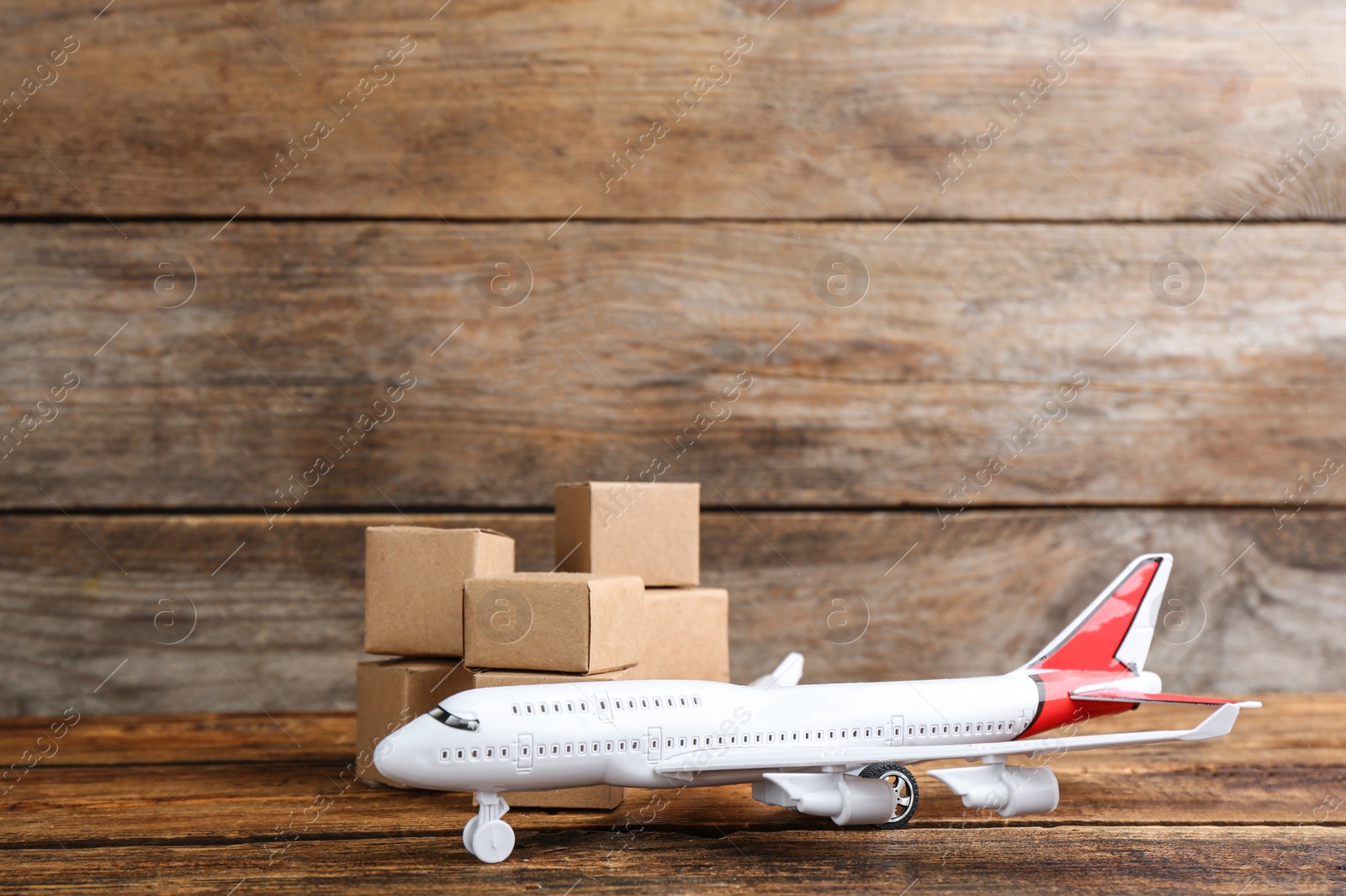 Photo of Airplane model and carton boxes on wooden background, space for text. Courier service