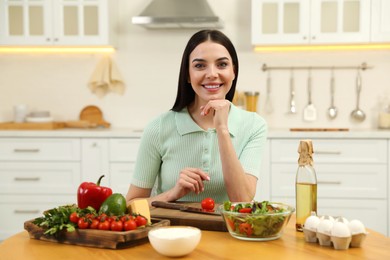 Photo of Happy woman cooking salad at table in kitchen. Keto diet