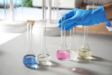 Photo of Scientist taking flask with colorful liquid from table indoors, closeup. Laboratory analysis