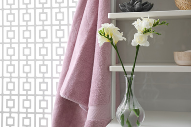 Photo of Shelving unit with beautiful white freesia flowers, towel and accessories indoors