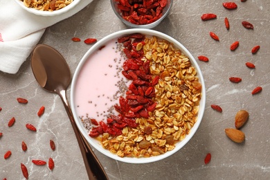 Photo of Smoothie bowl with goji berries and spoon on beige marble table, flat lay
