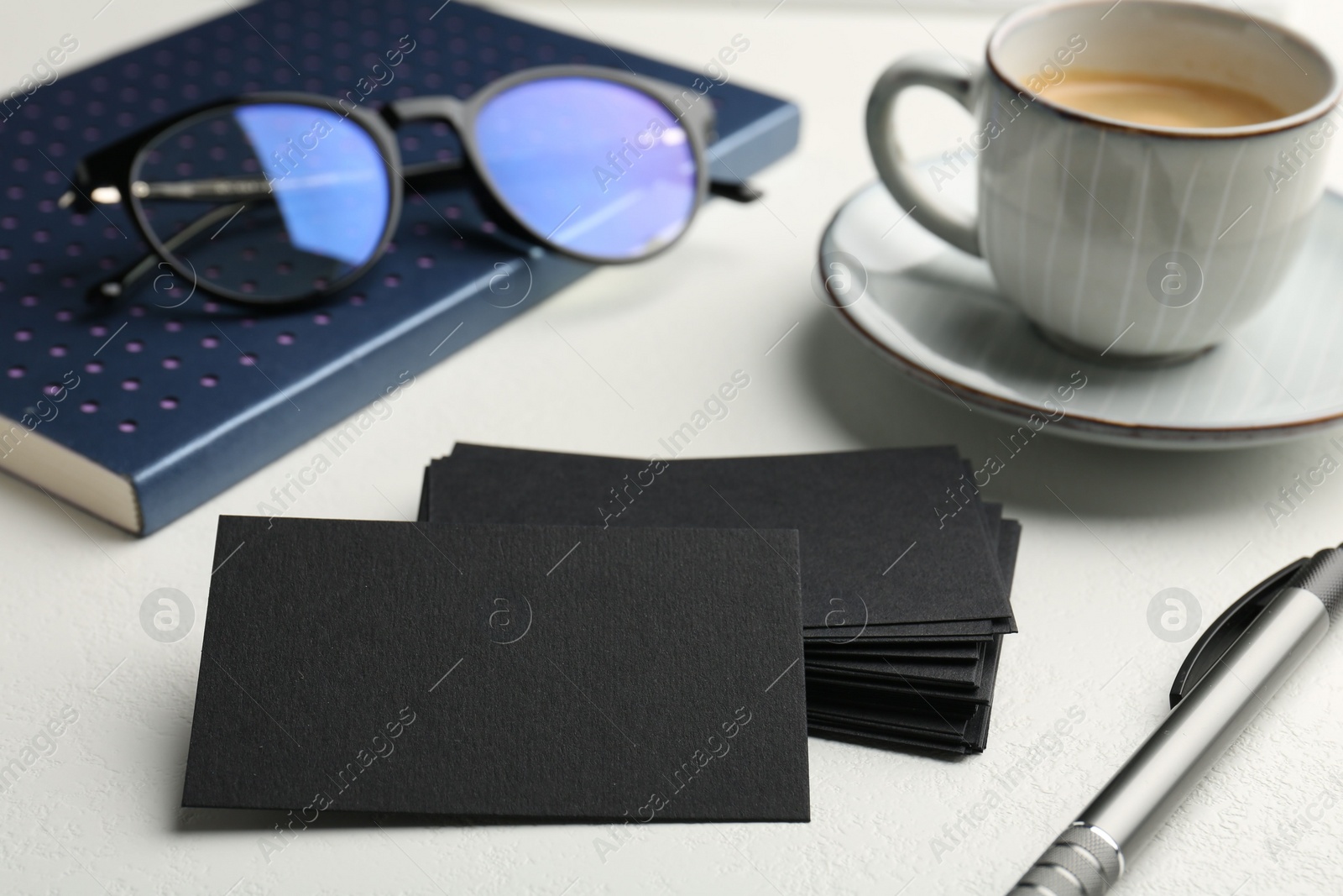 Photo of Blank black business cards, cup of coffee, glasses and stationery on white table, closeup. Mockup for design