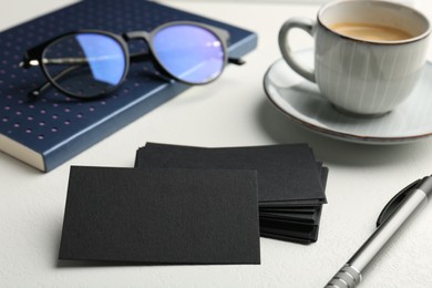 Photo of Blank black business cards, cup of coffee, glasses and stationery on white table, closeup. Mockup for design