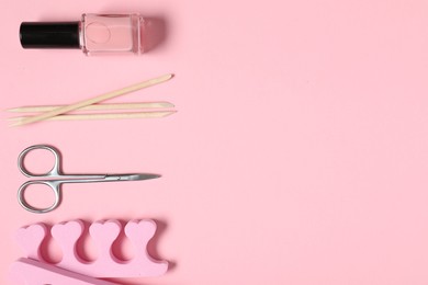 Photo of Nail polish, orange sticks, scissors and toe separators on pink background, flat lay. Space for text