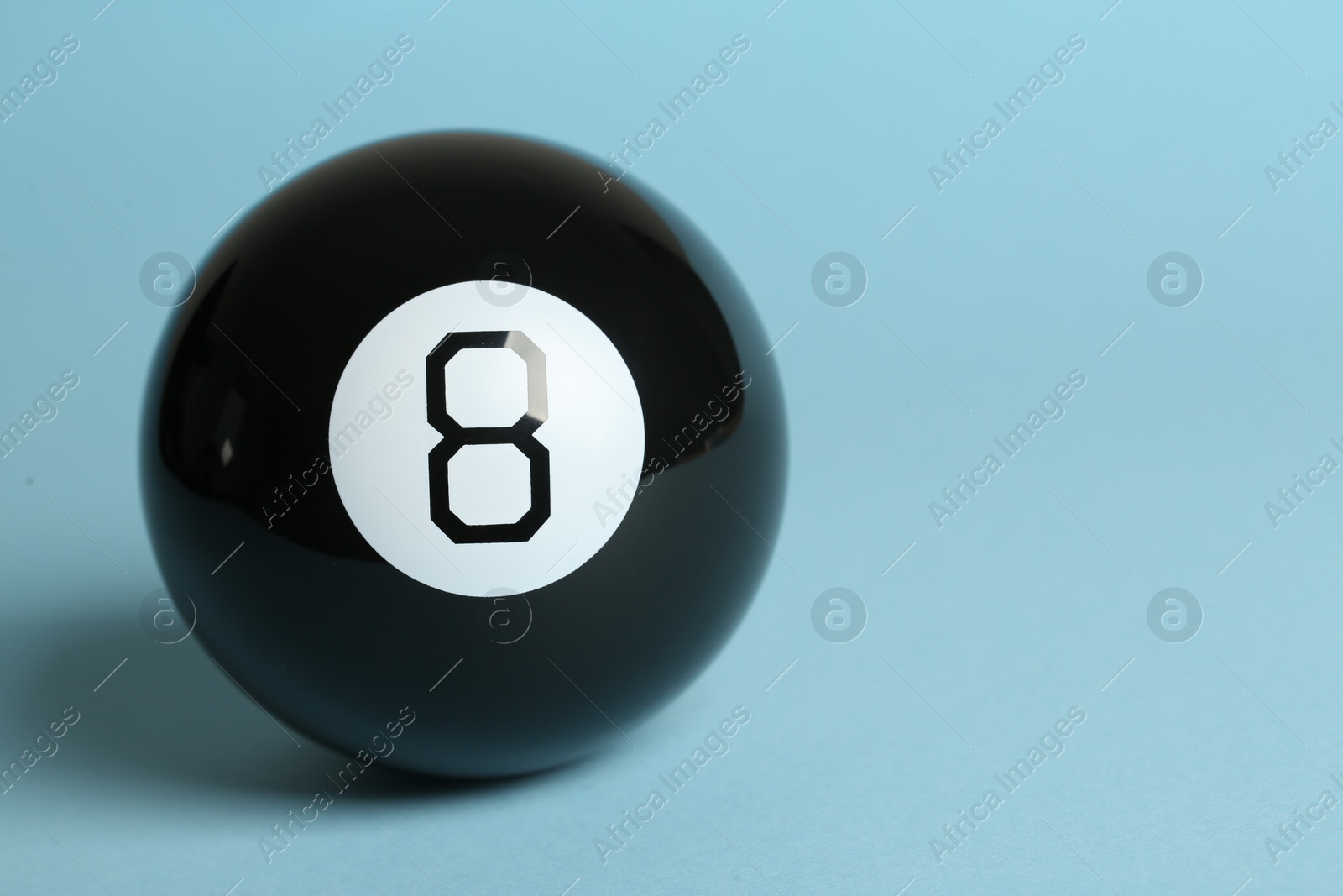 Photo of One magic eight ball on light blue background, space for text