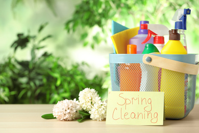 Photo of Card with words SPRING CLEANING, flowers and detergents on wooden table
