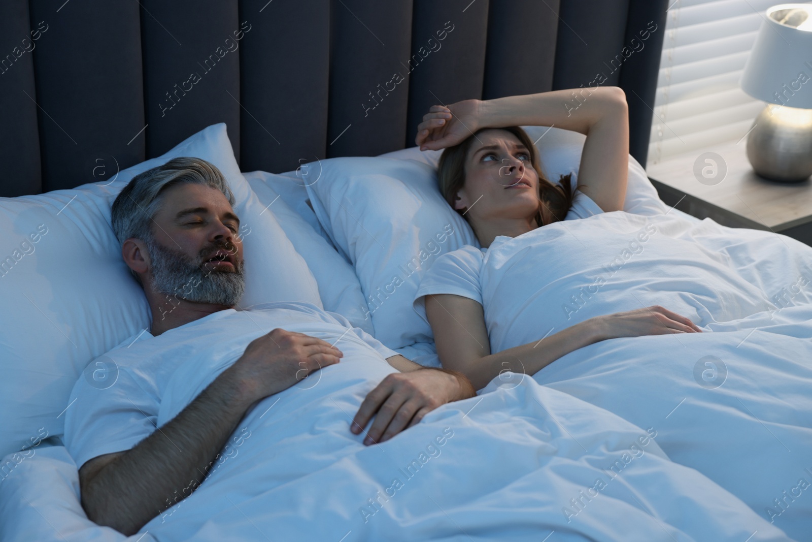 Photo of Irritated woman lying near her snoring husband in bed at home