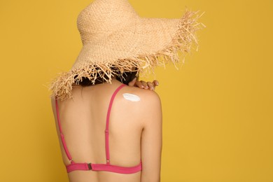 Photo of Teenage girl with sun protection cream on her back against yellow background